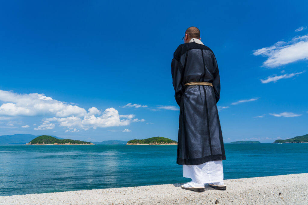 青空の下で海に向かって立つ僧侶の後ろ姿