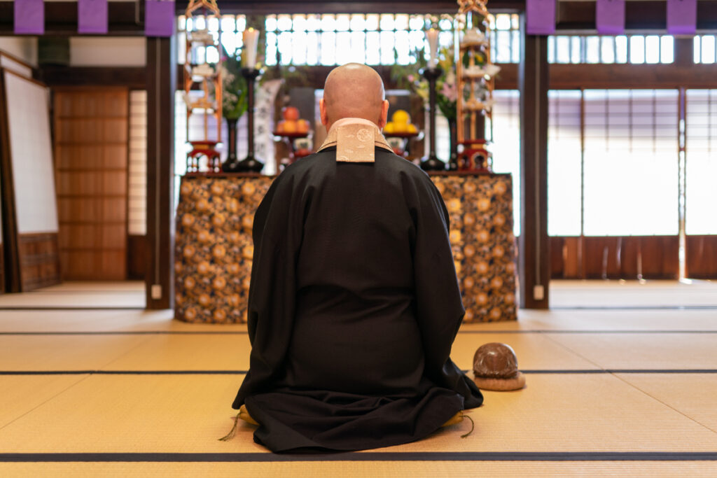 仏壇に向かって祈りをささげる僧侶の背中